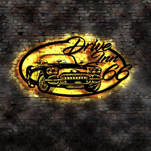 May include: A vintage-style neon sign with a black silhouette of a classic car and the text "Drive Inn 66" in a yellow oval shape against a brick wall background.