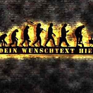 Op de afbeelding: Zwarte silhouet van de evolutie van de mens, eindigend met een man die tuiniert. Het silhouet bevindt zich op een zwart metalen bord met de tekst "DEIN WUNSCHTEXT HIER" in geel.