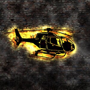 May include: A black silhouette of a helicopter against a brick wall with a yellow glow behind it.