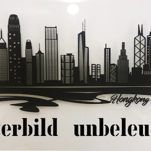 May include: Black silhouette of the Hong Kong skyline with the word "Hongkong" written underneath. The image is labelled "Musterbild unbeleuchtet" which translates to "Sample image unlit".