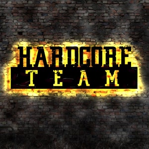 May include: A neon sign with the words "HARDCORE TEAM" in black letters on a yellow background. The sign is mounted on a brick wall.