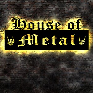 May include: A black sign with yellow lettering that reads "House of Metal" with a skeleton hand making the rock and roll sign on each side of the text.