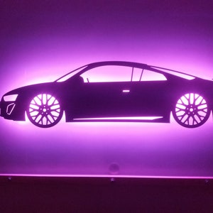 May include: A black silhouette of a car with a pink glow behind it. The car is a coupe with a sleek design and large wheels. The silhouette is mounted on a wall.