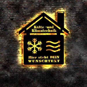 Op de afbeelding: Een zwart en geel bord in de vorm van een huis, met een sneeuwvlok en golvende lijnen. De tekst op het bord luidt "Kälte- und Klimatechnik" en "Hier steht DEIN WUNSCHTEXT".