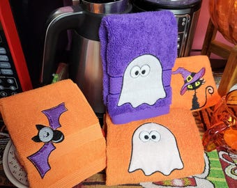 Könnte beinhalten: Vier Halloween-Küchenhandtücher mit gestickten Designs. Ein Handtuch ist lila mit einem weißen Geist, eines ist orange mit einer schwarzen Fledermaus und zwei sind orange mit weißen Geistern.