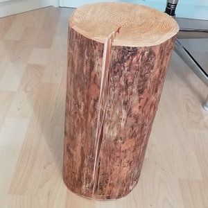 Könnte beinhalten: Ein rustikaler Holzhocker aus einem Baumstamm, der in zwei Hälften gespalten und mit einer natürlichen Oberfläche versehen wurde. Der Hocker steht auf einem hellen Holzboden.
