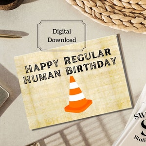 Peut inclure: Une carte imprimable téléchargeable numériquement avec un fond jaune et du texte noir qui dit "Happy Regular Human Birthday". Un cône de circulation noir et orange est au centre de la carte.