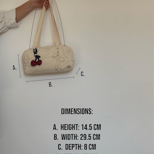 May include: A cream-colored handbag with black polka dots, featuring a cherry-shaped charm and a pearl-like bow accent. Dimensions are 14.5 cm in height, 29.5 cm in width, 8 cm in depth, and a 65 cm strap length as indicated in the image text.