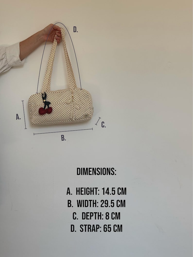May include: A cream-colored handbag with black polka dots, featuring a cherry-shaped charm and a pearl-like bow accent. Dimensions are 14.5 cm in height, 29.5 cm in width, 8 cm in depth, and a 65 cm strap length as indicated in the image text.