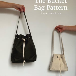 May include: A dark olive green bucket bag and a smaller off-white bucket bag, both featuring drawstring closures with white rope and silver-toned metal grommets. The text "The Bucket Bag Pattern Faye Studios" is visible in the upper right.