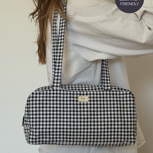 May include: A rectangular shoulder bag featuring a black and white gingham check pattern with two matching fabric straps. A small rectangular label with the text "loya studio" is centered on the front. A circular badge reads "CONFIDENT BEGINNER FRIENDLY".