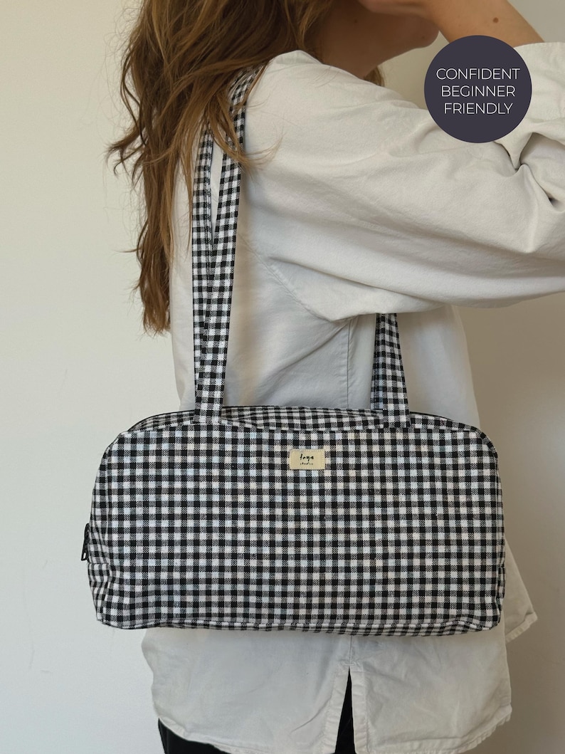 May include: A rectangular shoulder bag featuring a black and white gingham check pattern with two matching fabric straps. A small rectangular label with the text "loya studio" is centered on the front. A circular badge reads "CONFIDENT BEGINNER FRIENDLY".