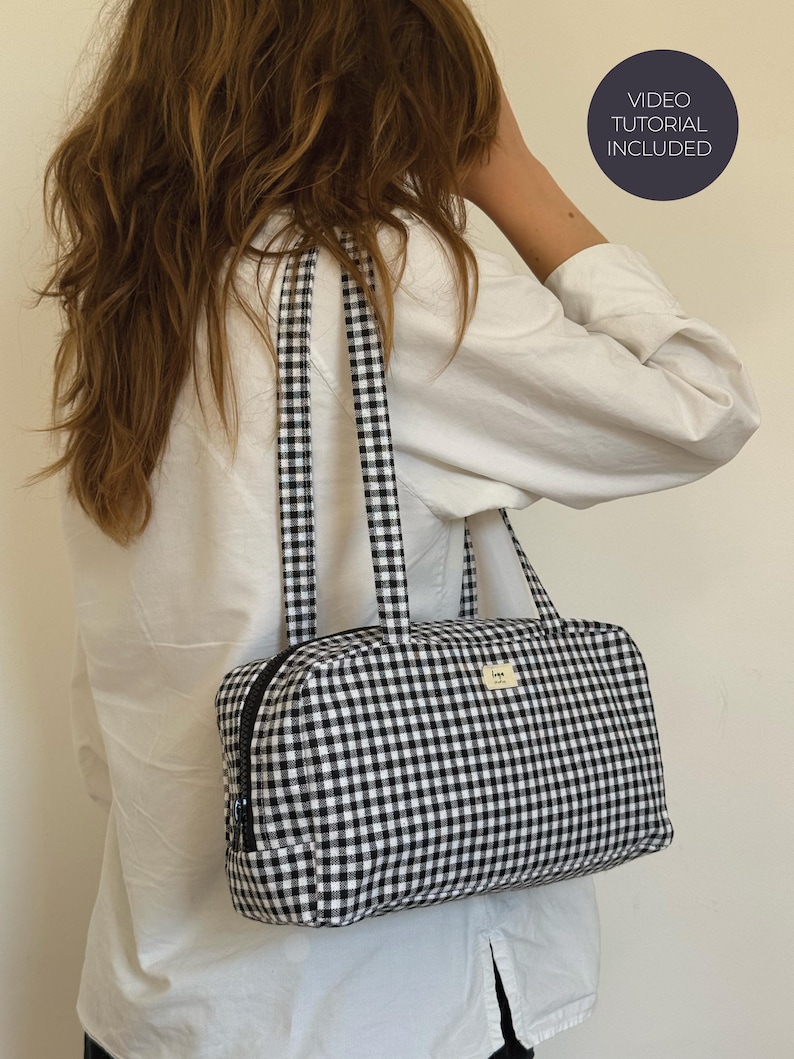 May include: A rectangular shoulder bag featuring a black and white gingham check pattern, two matching fabric straps, and a black zipper closure. A small rectangular label is attached to the front. A circular badge states VIDEO TUTORIAL INCLUDED.