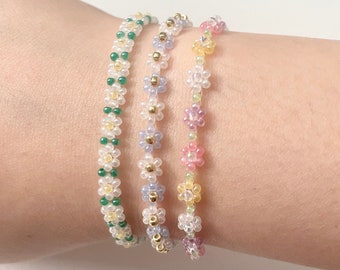 Puede incluir: Tres pulseras de cuentas con cuentas en forma de flor en verde, morado y rosa.