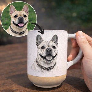 May include: A ceramic mug featuring a detailed illustration of a smiling French Bulldog. The mug has a white upper section and a tan base. The dog is wearing a patterned collar. A circular image of the dog is in the upper left corner.
