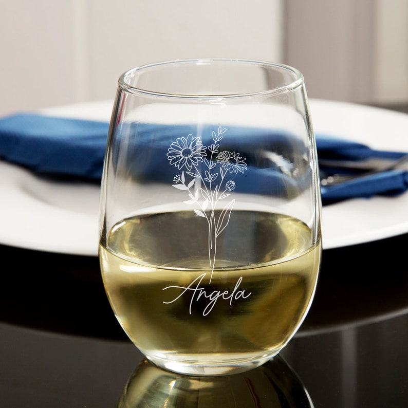 May include: A clear glass wine glass with a white floral design and the name "Angela" etched on the side.