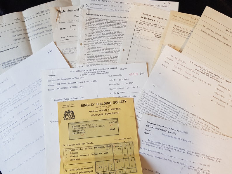 Op de afbeelding: Een verzameling vintage documenten, waaronder verzekeringspolissen en financi&euml;le overzichten, ligt verspreid. De papieren zijn verouderd met zichtbare kreukels en vervaagde inkt, wat duidt op historische waarde. De documenten bevatten tekst en diverse bedrijfslogo's.