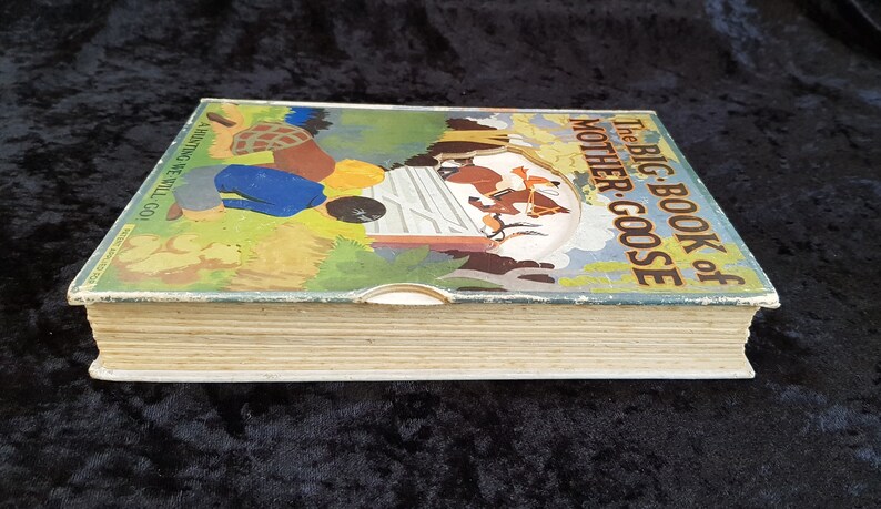 Op de afbeelding: Vintage kinderboek getiteld "The Big Book of Mother Goose". De omslag toont een kleurrijke illustratie van figuren en dieren in een landelijke sc&egrave;ne. De pagina's van het boek zijn verouderd en vertonen tekenen van slijtage.