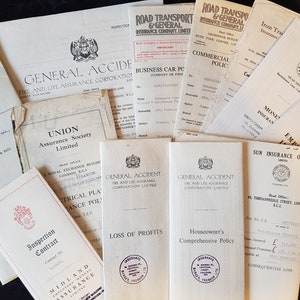 Op de afbeelding: Een verzameling vintage verzekeringsdocumenten, waaronder polissen en contracten, met diverse bedrijfslogo's en tekst. De documenten zijn in tinten wit en beige, met zwarte tekst en enkele rode accenten. Gerangschikt op een donkere ondergrond.