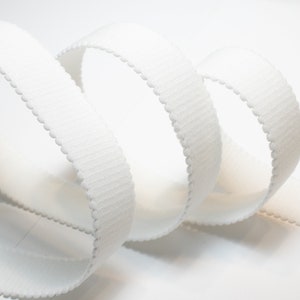 May include: White elastic trim with a scalloped edge. The trim is ribbed and has a soft, flexible texture.