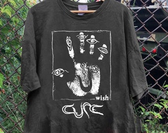 Puede incluir: Una camiseta verde oscuro con una impresión blanca de una mano con ojos y el texto "wish" y "The Cure".