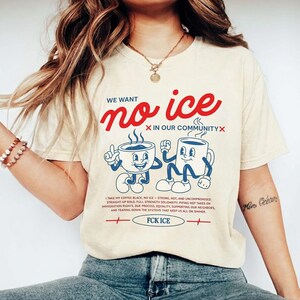Puede incluir: Camiseta color crema con el texto "WE WANT no ice" en escritura roja. Debajo, dos tazas de caf&eacute; de dibujos animados. La camiseta tambi&eacute;n presenta texto sobre los derechos de inmigraci&oacute;n y la frase "FCK ICE."