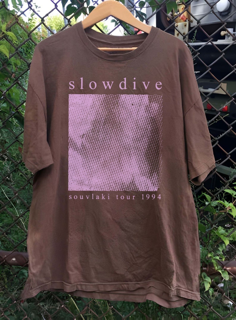 May include: A brown t-shirt with a pink and white graphic print of a face and the text "slowdive souvlaki tour 1994".