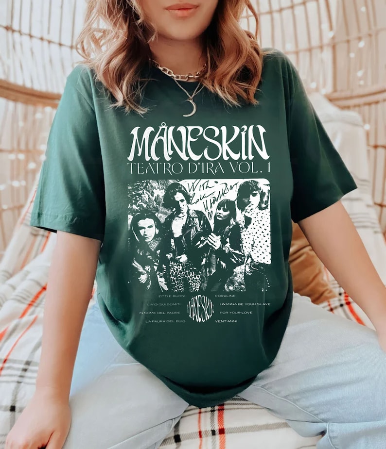 May include: A dark green t-shirt with a white graphic print of the band M&aring;neskin. The graphic includes the band's name, the album title "Teatro d'Ira Vol. I", and a black and white image of the band members. The text "With Love & Thunder" is written in white above the band's image. The song titles "Zitti e buoni", "I Wanna Be Your Slave", "Coraline", "For Your Love", "In Nome Del Padre", "La Paura Del Buio", and "Vent'anni" are listed below the band's image.