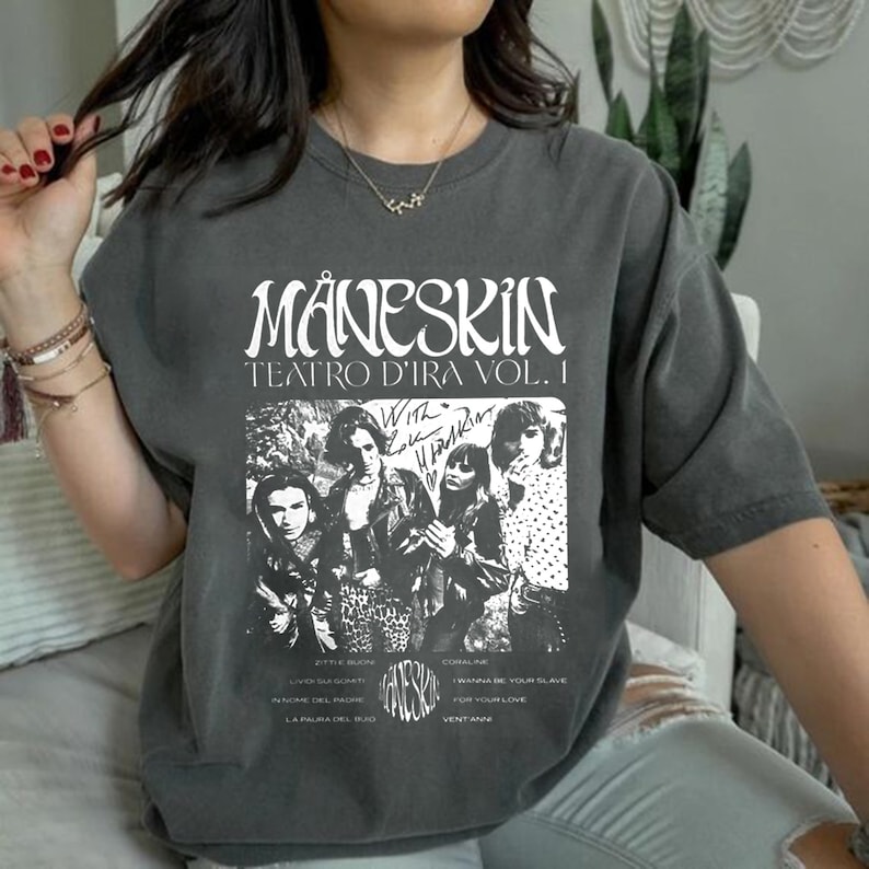 May include: A gray t-shirt with a black and white graphic print of the band M&aring;neskin. The graphic includes the band's name, the album title "Teatro d'Ira Vol. I", and a photo of the band members. The text on the shirt reads "With Love, M&aring;neskin".