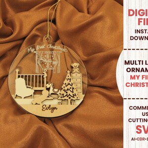 May include: A multi-layer wooden ornament for a baby's first Christmas. The ornament is round and features a crib, rocking horse, Christmas tree, and a teddy bear. The text "My first Christmas" and the name "Evlyn" are engraved on the ornament.
