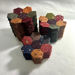 Peut inclure: Une pile de pièces de tissu hexagonales de différentes couleurs et motifs, notamment rouge, vert, marron et bleu. Les pièces de tissu sont cousues ensemble pour créer un motif en forme de fleur.