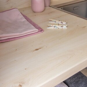 May include: A light-colored wooden countertop with a sink, two pink towels, two decorative pink vases, and two clothespins. The clothespins are white with colorful polka dots. The towels are folded neatly.