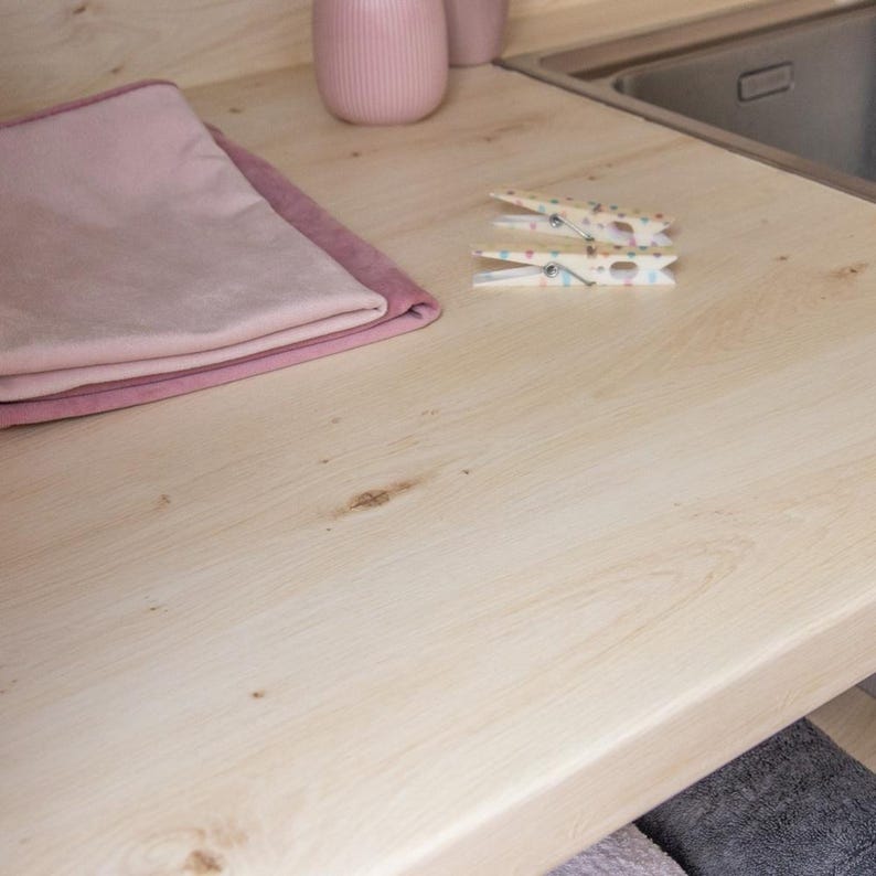 May include: A light-colored wooden countertop with a sink, two pink towels, two decorative pink vases, and two clothespins. The clothespins are white with colorful polka dots. The towels are folded neatly.