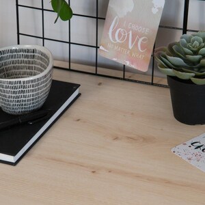 May include: A desk scene featuring a black and white patterned ceramic bowl, a black notebook with a pen, a small potted succulent, and a card that reads "I choose love no matter what." The background includes a black wire grid.
