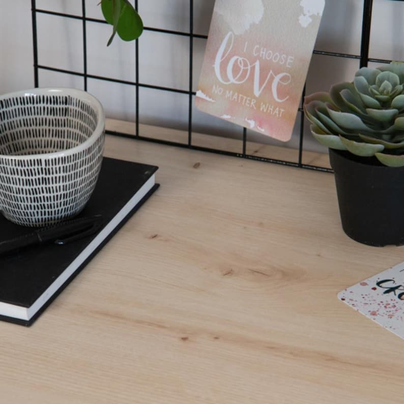 May include: A desk scene featuring a black and white patterned ceramic bowl, a black notebook with a pen, a small potted succulent, and a card that reads "I choose love no matter what." The background includes a black wire grid.