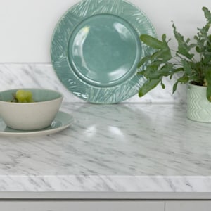 Puede incluir: Un plato de cerámica verde azulado con un borde texturizado se encuentra junto a un cuenco pequeño con uvas. También se ven un platillo a juego y una planta en maceta. Los artículos están sobre una encimera de mármol blanco.