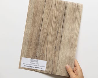 May include: A rectangular sample of Sanremo Oak flooring featuring a light brown wood grain pattern. A white sticker in the bottom left corner displays the text: CREATE YOUR WORLD, SANREMO OAK, Thank you for purchasing this sample, www.createyourworld.co.uk.