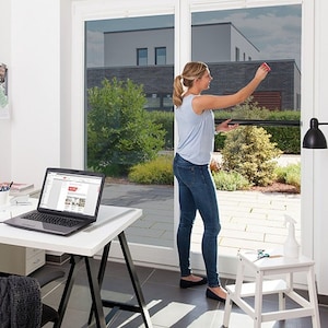 May include: A retractable black window screen installed on a large glass door. The screen features a dark mesh material that pulls down from the top frame, providing a barrier while maintaining visibility of the outdoor area through the glass.
