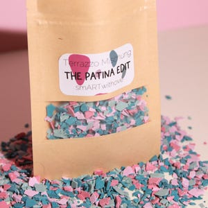 Könnte beinhalten: Ein Kraftpapierbeutel mit einem transparenten Fenster, das farbige Terrazzostücke zeigt. Das Etikett lautet "Terrazzo Mischung THE PATINA EDIT smartwithove". Die Stücke sind rosa, blau und türkis.