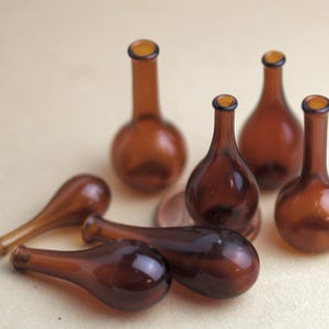 Könnte beinhalten: Eine Sammlung kleiner, brauner Glasflaschen mit runden Körpern und schmalen Hälsen. Die Flaschen variieren in Form und Größe, einige liegen auf der Seite. Das Glas hat einen warmen, bernsteinfarbenen Farbton.