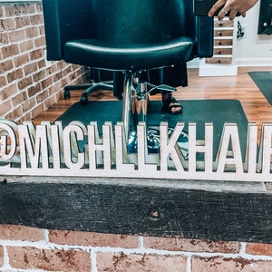 May include: A wooden sign with the text "@michilkhaird" in a salon setting. The sign is sitting on a windowsill with a brick wall behind it.