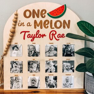 Może przedstawiać: Drewniany znak z tekstem "One in a Melon Taylor Rae" i wyciętym czerwonym arbuzem. Znak ma 12 miejsc na zdjęcia z czarno-białymi zdjęciami dziecka w r&oacute;żnym wieku.