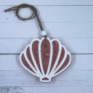 May include: A brown seashell ornament with white detailing, hanging from a twine string with a white bead.