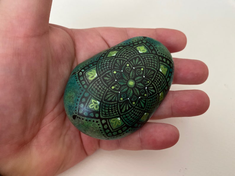 Hand drawn mandala natural stone rock with green background.