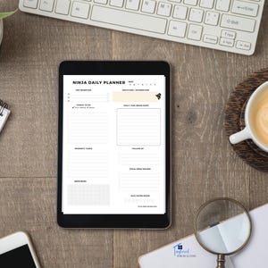 Op de afbeelding: Een zwarte tablet met een witte dagelijkse planner op het scherm. De planner is onderverdeeld in secties voor topprioriteiten, taken, prospecttaken, follow-up, snelle notities, social media tracker, dagelijkse waterinname, dankbaarheid/bevestiging en dagelijkse braindump. De tablet ligt op een houten oppervlak met een toetsenbord, een kopje koffie en een vergrootglas.