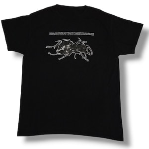 以下が含まれることがあります： 黒いTシャツに、白い甲虫のグラフィックと「Massive Attack Mezzanine」の文字がプリントされています。