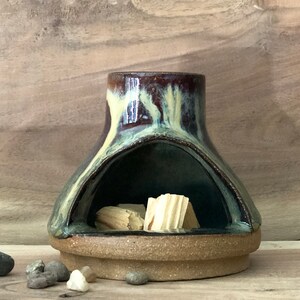 Puede incluir: Un quemador de incienso de cer&aacute;mica con un esmalte marr&oacute;n oscuro, verde y amarillo. El quemador tiene una gran abertura en la parte delantera y una abertura m&aacute;s peque&ntilde;a en la parte superior. Hay varillas de incienso de madera dentro del quemador.