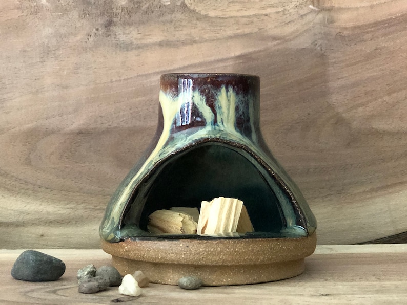 Puede incluir: Un quemador de incienso de cer&aacute;mica con un esmalte marr&oacute;n oscuro, verde y amarillo. El quemador tiene una gran abertura en la parte delantera y una abertura m&aacute;s peque&ntilde;a en la parte superior. Hay varillas de incienso de madera dentro del quemador.