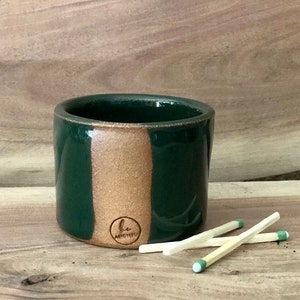 Puede incluir: Un rascador de cerillas de cerámica verde y marrón con un logotipo marrón que dice "b. archite"