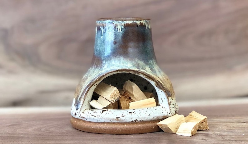Puede incluir: Un quemador de incienso de cer&aacute;mica con un esmalte azul y marr&oacute;n. El quemador tiene una peque&ntilde;a abertura en la parte delantera para sostener varillas de incienso. El quemador est&aacute; lleno de astillas de madera.